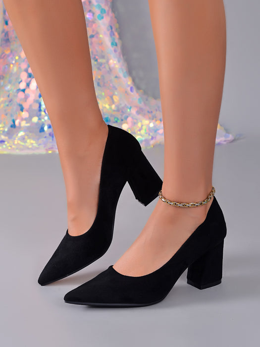 Black pointed-toe block-heel pumps worn on a model's feet, featuring a suede-like finish and a delicate gold-toned rhinestone ankle bracelet.