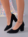 Black pointed-toe block-heel pumps worn on a model's feet, featuring a suede-like finish and a delicate gold-toned rhinestone ankle bracelet.