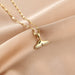 A gold chain necklace with a mermaid tail pendant adorned with small clear stones, displayed on draped beige satin fabric.