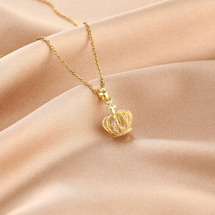 Gold crown-shaped pendant necklace on a soft pink fabric background