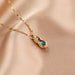 A gold chain necklace with a pear-shaped pendant featuring a sparkling blue gemstone and a small rose-gold accent, displayed on a soft beige satin fabric.