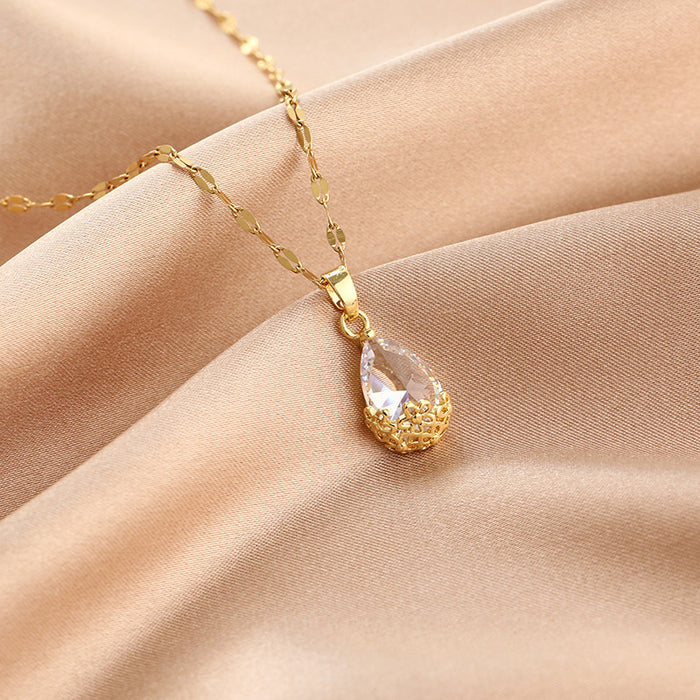 Gold necklace with a teardrop-shaped pendant on a beige fabric background