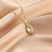 Gold necklace with a teardrop-shaped pendant on a beige fabric background