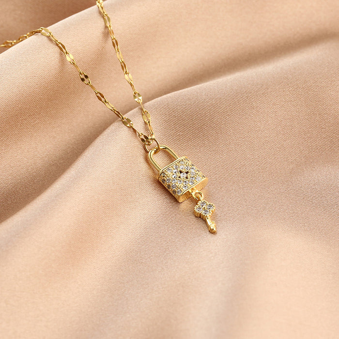 A gold-toned necklace with a padlock pendant encrusted with clear stones and a dangling key charm, displayed on draped beige satin fabric.