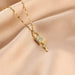 A gold-toned necklace with a padlock pendant encrusted with clear stones and a dangling key charm, displayed on draped beige satin fabric.