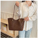 A person wearing a cream button-up shirt and light blue jeans holds a brown leopard-print tote bag with dark brown shoulder straps in an indoor room setting.