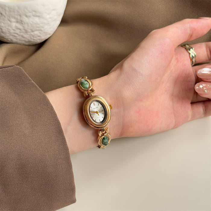 Gold watch with green gemstones on a wrist against a neutral background