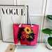Tote bag with a design of a woman with flowers in her hair on a pink background, placed on a surface with a 'Vogue' magazine in the background.