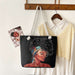 Black tote bag with a colorful design of a woman's face, hanging on a wooden hook with a white shirt and photo album in the background.