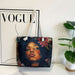 Tote bag with a design of a woman's face and flowers on a surface with a 'Vogue' magazine in the background.
