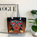 Tote bag with artistic design of a woman wearing sunglasses and holding 'WOAH' in front of her eyes, placed on top of a Vogue magazine.