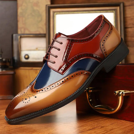 A men's three-color brogue oxford shoe with a glossy finish, featuring tan, brown, and navy panels, resting on a wooden surface with vintage props in the background.