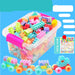 Multicolor particle building blocks in a clear plastic storage bin with a pink handle, shown on a bright blue background with Chinese promotional text and small toy train examples.