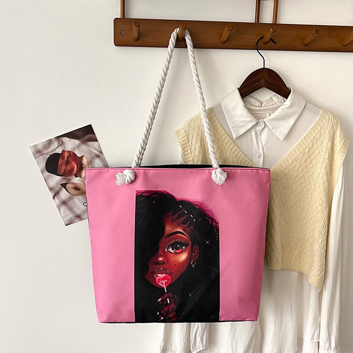 Pink tote bag with a graphic design of a face, hanging on a coat rack with clothes in the background.