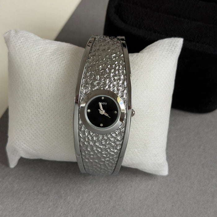 A silver-toned women's watch with a textured, hammered metal band and a black dial, displayed on a white textured cushion.