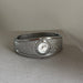 A silver-toned wide cuff bracelet watch with a textured, hammered outer band, a polished inner lining, and a small round white dial face.