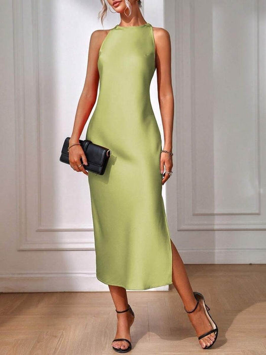 Woman wearing a green dress with a black clutch against a white wall.