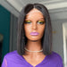 Mannequin head with a black bob wig and purple top, wearing yellow eyeshadow and pink lipstick.