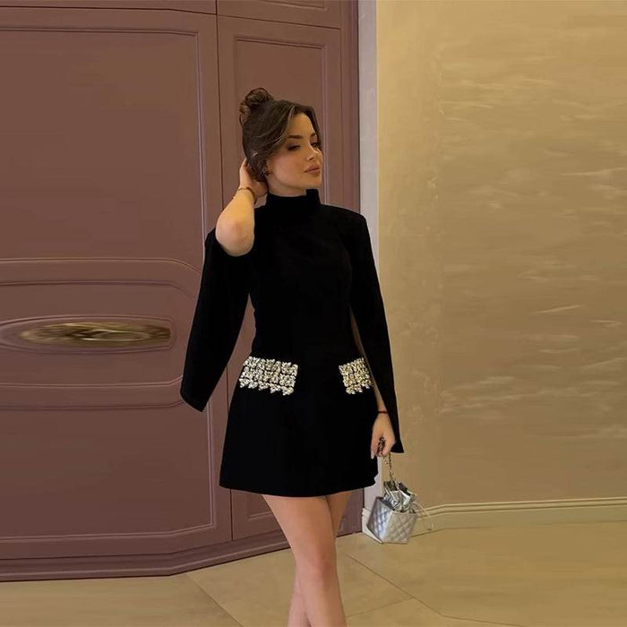 Woman in a black dress with silver embellishments standing against a beige wall.