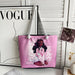 Pink tote bag with a character design on a surface with a 'Vogue' magazine in the background.