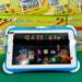 A kids tablet PC with a blue and white protective bumper case, displaying the SAIL Air operating system on its screen. The tablet is positioned in front of its colorful product packaging boxes on a green surface.