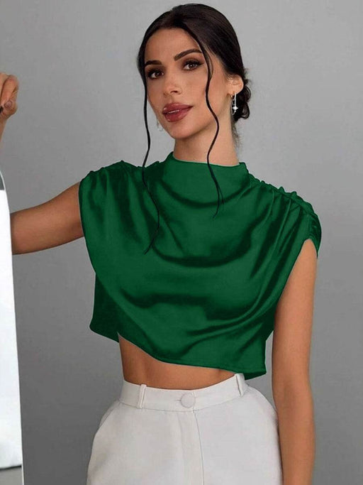 Woman wearing a green top and white pants against a gray background