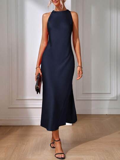 Woman wearing a navy blue dress holding a clutch against a white paneled wall.