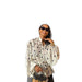 A woman wearing a white long-sleeve blouse with black polka dots, black sunglasses, and a black handbag, set against a plain white background.