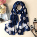 Navy blue scarf with white floral patterns on a beige surface with flowers and a magazine.
