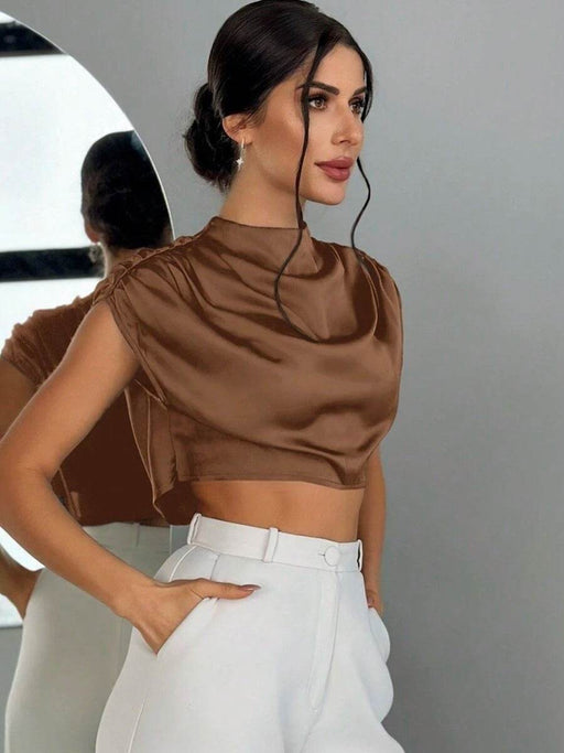 Woman wearing a brown top and white pants against a neutral background