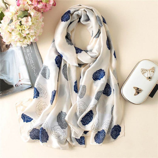White scarf with blue floral patterns on a light surface with flowers and a handbag.