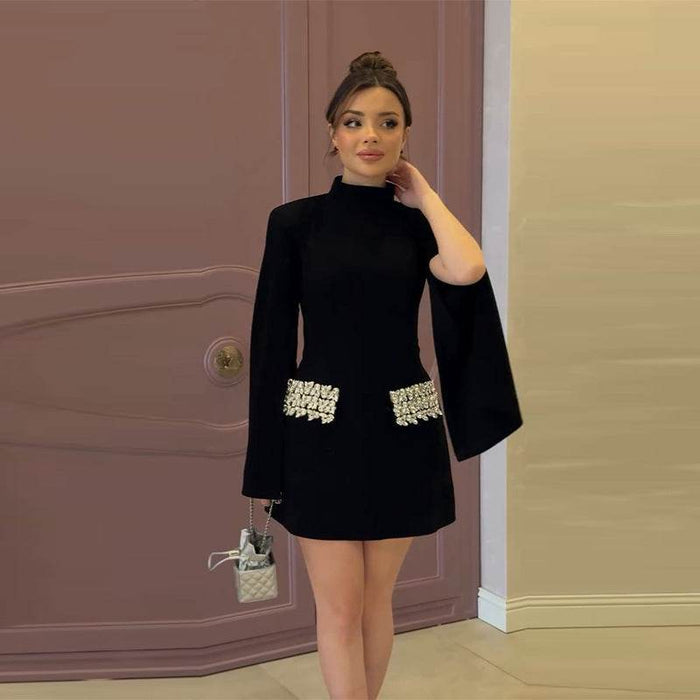 Woman wearing a black dress with bell sleeves and embellishments in front of a door.