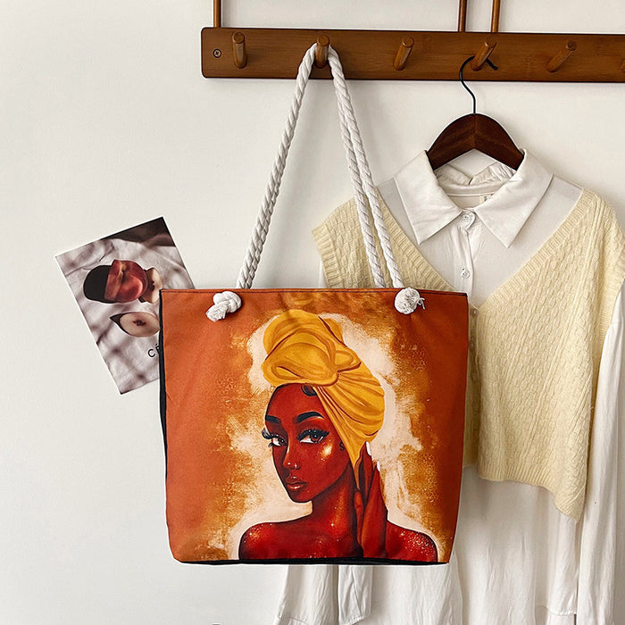 Tote bag with a painted design of a woman with a yellow headscarf, hanging on a wooden rack with other items.