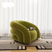 Green armchair on a patterned rug with white curtains in the background