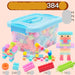 A colorful children's building block set in a translucent storage box with a light blue lid, shown with several example constructions and text indicating the set contains about 384 large-grained blocks plus included accessories on a pale pink background.