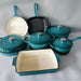 Collection of teal cookware including pots, pans, and a bread box on a white surface.