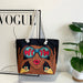 Tote bag with artistic design of a woman wearing sunglasses and holding 'WOAH' in front of her eyes, placed on top of a Vogue magazine.