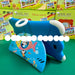 A blue shark-shaped tablet stand holding a tablet, with colorful SAIL Air 7.0 Kids Tablet PC retail boxes stacked behind it on a green surface.