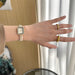 Hand wearing a pearl bracelet with a watch and gold ring, against a neutral background
