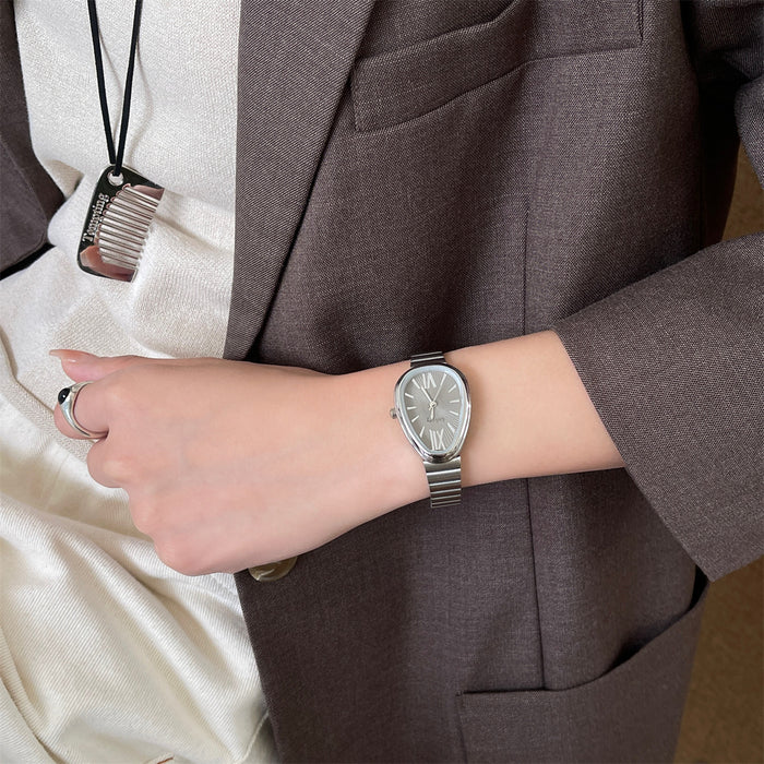 A silver-toned analog watch with a matching metal link bracelet worn on a person's wrist, shown against a brown blazer and cream satin blouse.