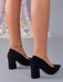 Black pointed-toe block-heel pumps shown on a model's feet, featuring a suede-like finish and a silver rhinestone anklet.