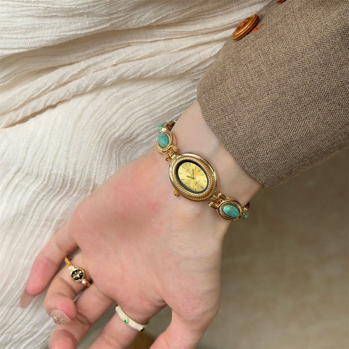 Gold wristwatch with turquoise stones on a wrist against a neutral background