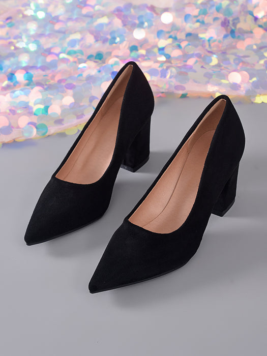 A pair of black pointed-toe high heels with block heels, shown on a gray surface with a sparkling multicolor background.