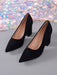 A pair of black pointed-toe high heels with block heels, shown on a gray surface with a sparkling multicolor background.