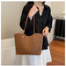 A person wearing a black button-up shirt and white skirt holds a large brown leopard-print tote bag with tan shoulder straps and gold-tone hardware in an indoor room setting.