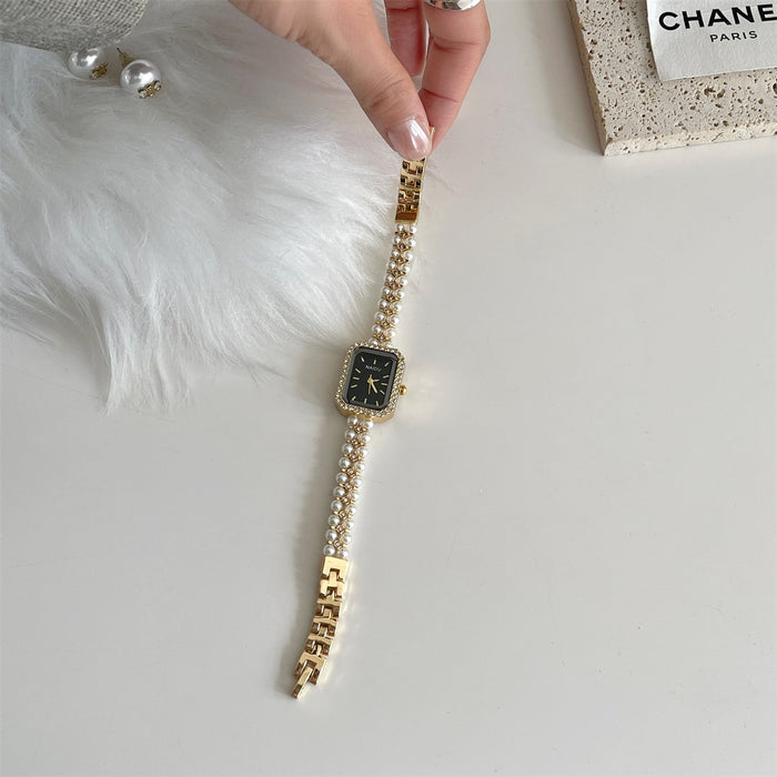 Gold watch with a black face on a white surface, with a Chanel box in the background.