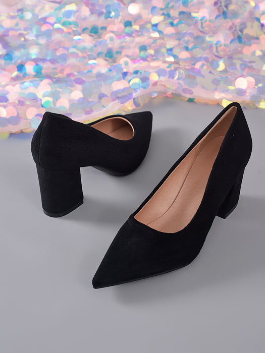 A pair of black pointed-toe high heels with block heels, shown on a gray surface with a sparkling multicolor backdrop.