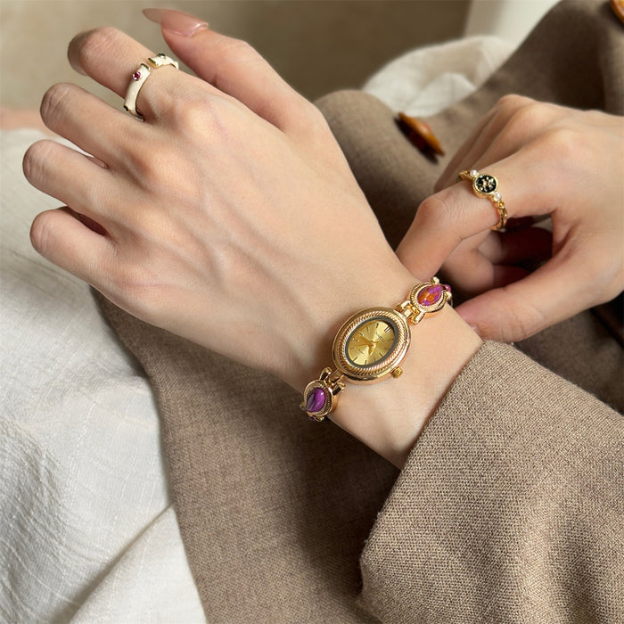 Close-up of a hand wearing a gold watch with gemstones on a neutral background