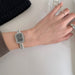 Hand wearing a silver watch with a plain background