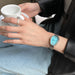 Person wearing a watch with a blue face, holding a white mug.